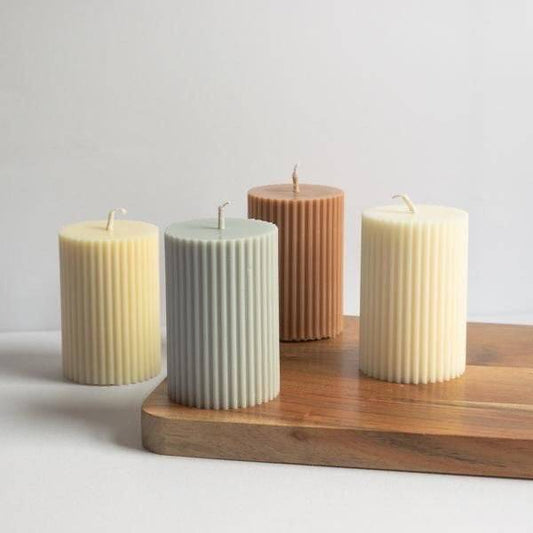 Set of ribbed pillar candles in neutral tones on a wooden tray, perfect for an outdoor candle display. Nature-inspired decor for a warm ambiance.